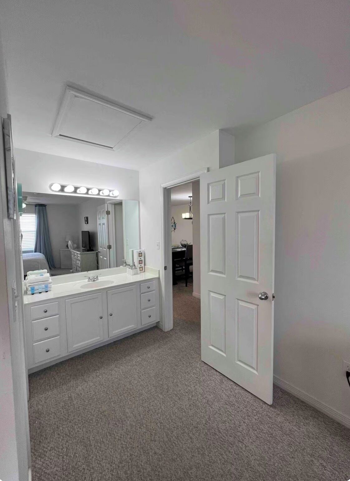 Une salle de bain moderne avec un grand meuble-lavabo, un miroir avec éclairage intégré et une porte donnant sur une autre pièce.