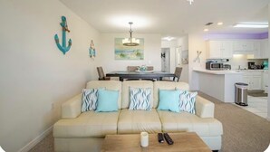 Ein Wohnzimmer mit einem beigefarbenen Sofa, einem Holztisch und einem Essbereich mit Tisch und Stühlen.
