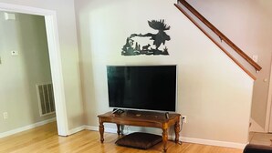 Een woonkamer met een houten salontafel, een flatscreen televisie op een standaard, een bank en een decoratie aan de muur.
