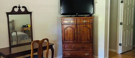 A bedroom with a bed, a wooden dresser, a television, a ceiling fan, and a door.