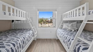 A room with two bunk beds, a window with a view of palm trees and a building, and a wooden floor. - Waterfront 3 Bedroom Condo with Beach Access Walkable to Everything. (Englewood)