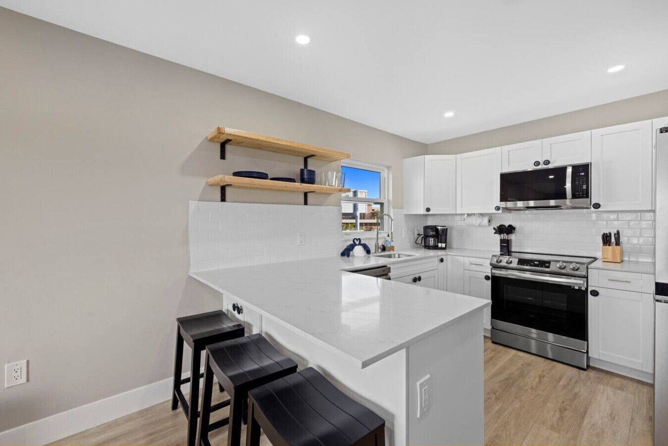 Una cocina moderna con armarios blancos, una isla central con taburetes, microondas, estufa y cafetera.
