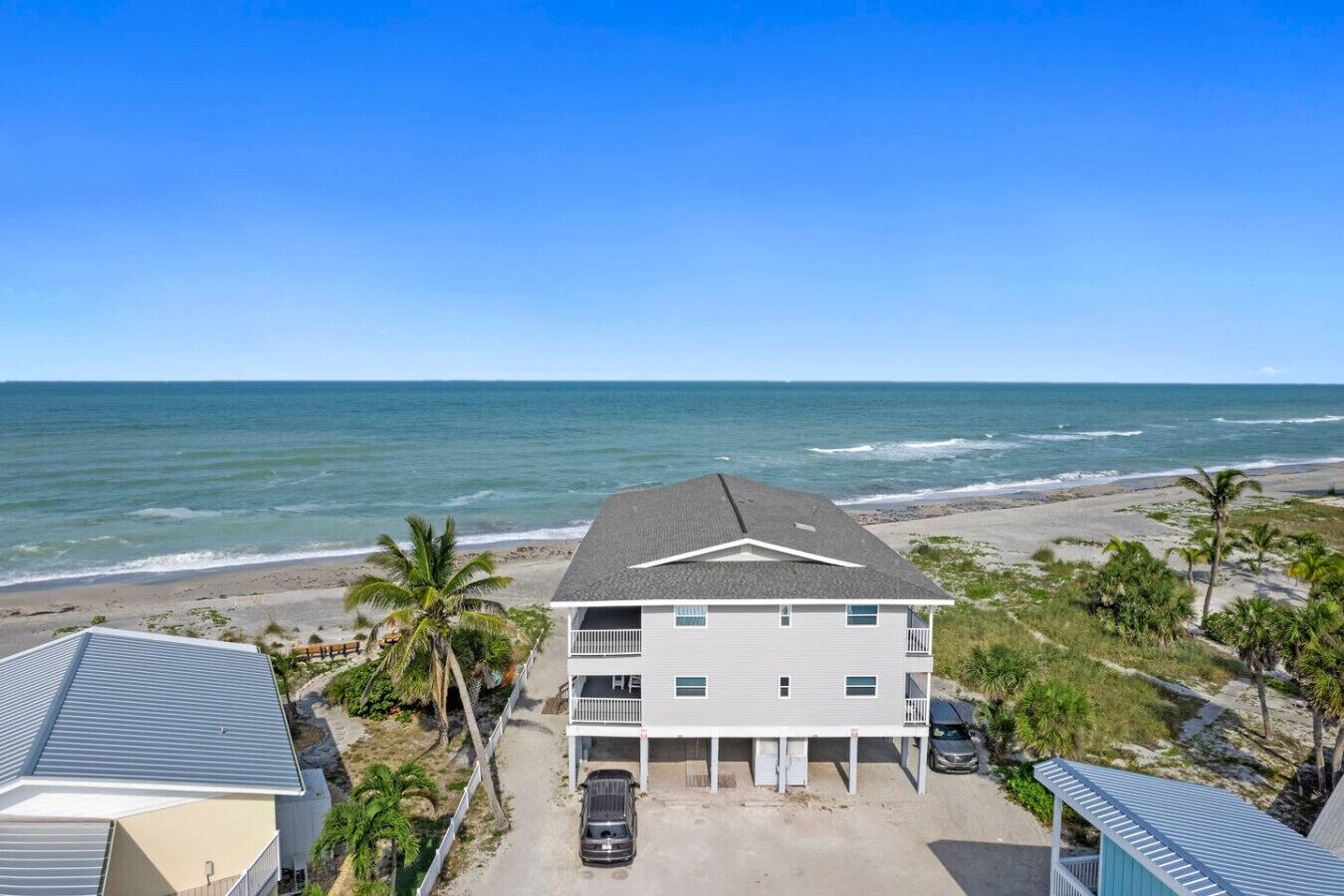 A beachfront property with a two-story building, a covered parking area, and a view of the ocean.
