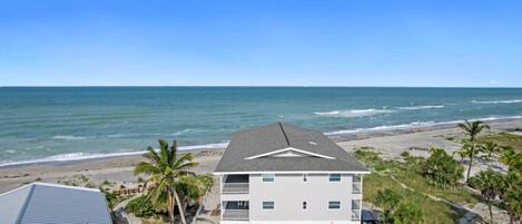A beachfront property with a two-story building, a covered parking area, and a view of the ocean.