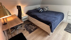 Makuuhuoneessa on sänky, kirjoituspöytä, jossa on lamppu, tuoli ja pieni matto.
