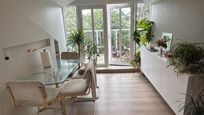 Moderni keittiö, jossa on lasinen ruokapöytä, kaksi tuolia, valkoinen kaappi, jossa on kasveja, ja näkymä suurten lasiovien läpi.