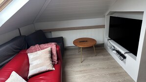 Moderni olohuone, jossa on punainen nahkasohva, pyöreä puinen sohvapöytä, suuri litteänäyttöinen televisio, joka on kiinnitetty seinään, ja kattoikkuna yläpuolella.