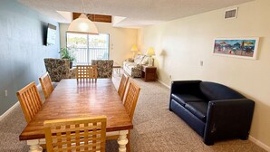 A dining area with a wooden table and chairs, a black sofa, and a painting on the wall. - Waterfront Condo w/Private Beach on Manasota Key! (Englewood)