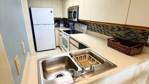A kitchen with a stainless steel sink, a microwave, a stove, and a refrigerator. - Bayfront 2-Bedroom Condo with Private Beach - 314 (Englewood)