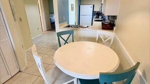 A dining area with a round table, four chairs, a hanging light fixture, and a kitchen in the background. - Bayfront 2-Bedroom Condo with Private Beach - 314 (Englewood)