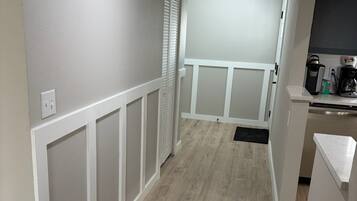 A hallway with a wooden floor, white walls, and a white door leading to a kitchen area.