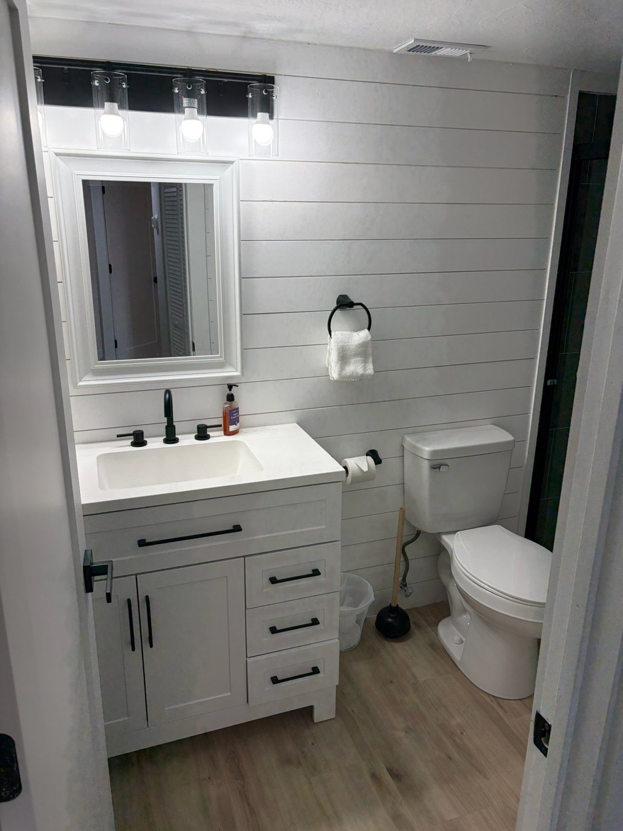 Une salle de bain avec un meuble-lavabo blanc, un miroir, des toilettes et un espace douche.