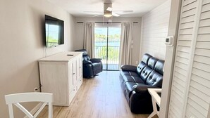 A compact living space with a dining area, a sofa set, a TV mounted on the wall, and a sliding door leading to a balcony. - Bayfront Condo with Private Beach - Unit 313 (Englewood)