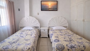 Une chambre avec deux lits simples, une table de chevet, un tableau accroché au mur et une armoire.