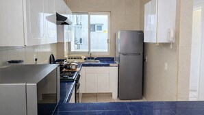 A compact kitchen with a stove, sink, and refrigerator, featuring a window with a view of the outside. - Spacious 3BR Apt | 2 Min to Sailfish Monument | Private Parking (Manzanillo)