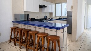A kitchen with a blue-tiled island, white cabinets, a stove, and wooden stools. - Spacious 3BR Apt | 2 Min to Sailfish Monument | Private Parking (Manzanillo)