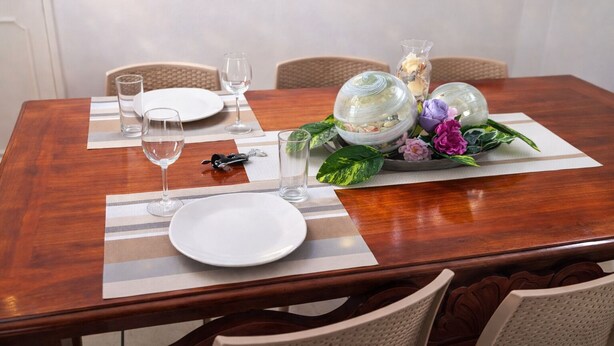 A dining table set with plates, glasses, a bottle opener, and a decorative centerpiece with flowers and leaves. - Spacious 3BR Apt | 2 Min to Sailfish Monument | Private Parking (Manzanillo)