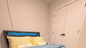 Een slaapkamer met een bed, een hoofdeinde met blauwe LED-verlichting, een grijze spreidek en een houten vloer.