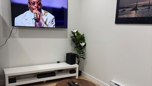 Een moderne woonkamer met een flatscreen televisie, een wit tv-meubel, een ronde salontafel, een getextureerd vloerkleed en een bank.