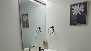 Een badkamer met een witte wasbak, een zwarte kraan en een spiegel erboven. Er zijn twee handdoekhouders aan de muur bevestigd, en een toilet is links zichtbaar.