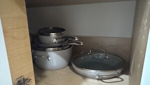 Een keukenkastje met roestvrijstalen kookgerei, waaronder pannen en een koekenpan.