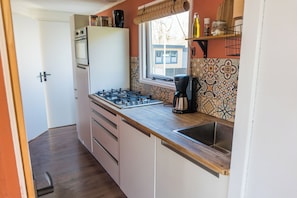 A compact kitchen with a gas stove, a coffee maker, and a window with a view of a building outside.