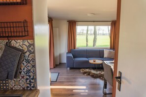Un salon moderne avec un canapé, une petite table ronde et une vue sur un champ verdoyant, visible à travers de grandes fenêtres.