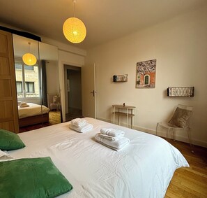 A hotel room with a bed, a green pillow, a hanging light fixture, a painting, and a chair.