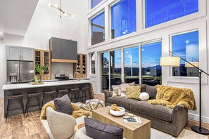 A modern kitchen with a central island, bar stools, and a large window overlooking a cityscape. - NEW Smoky Mtn Escape Luxe Cabin Pool Epic View (Sevierville)