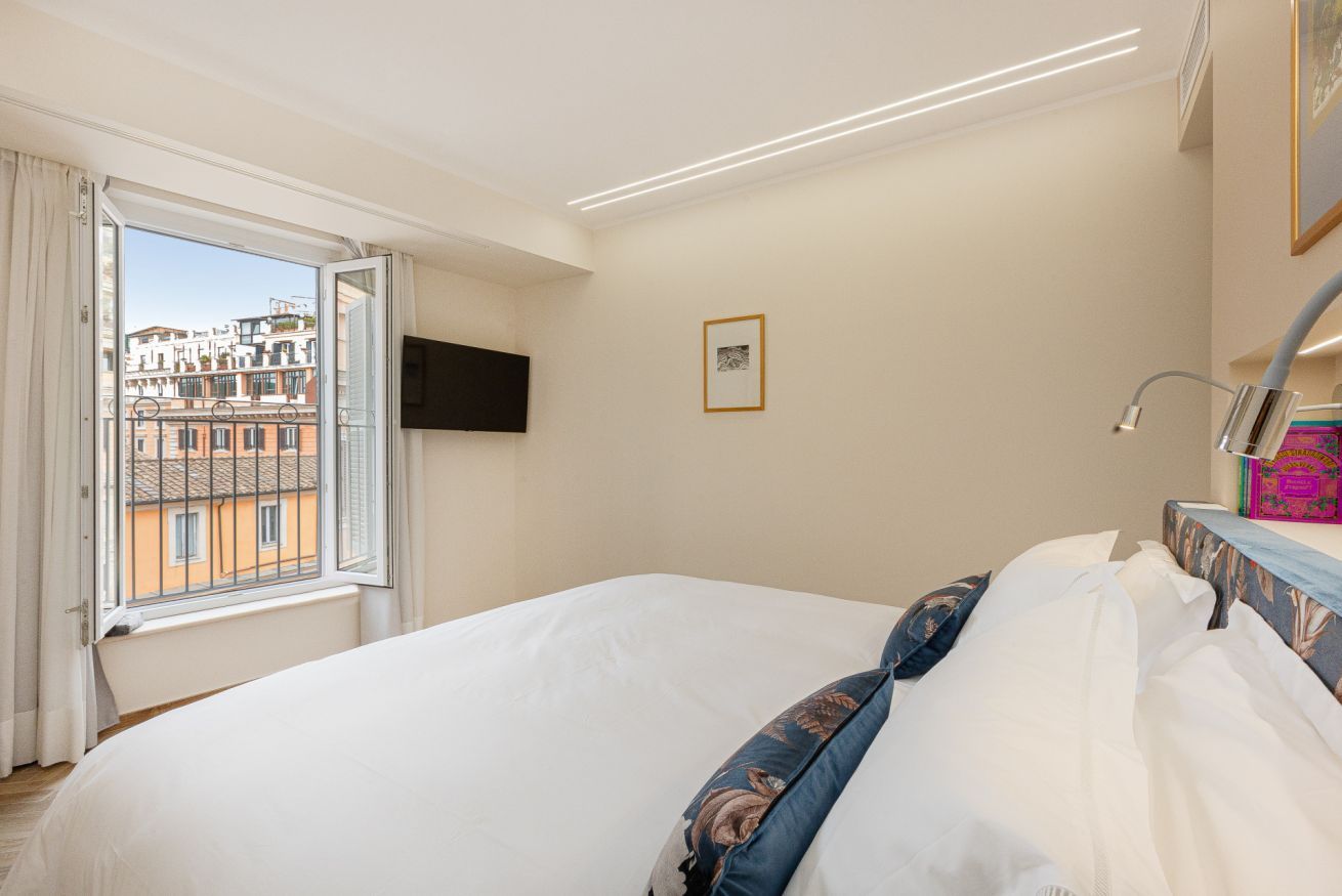 A bedroom with a large bed, a window with curtains, a flat-screen TV, and a framed picture on the wall.