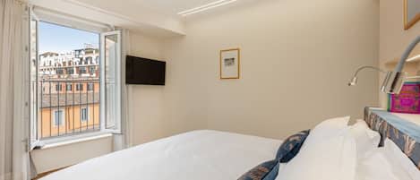 A bedroom with a large bed, a window with curtains, a flat-screen TV, and a framed picture on the wall.