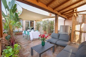 Eine Terrasse im Freien mit einer Couch, einem Tisch und Stühlen, umgeben von Blumentöpfen und einem Fernseher.