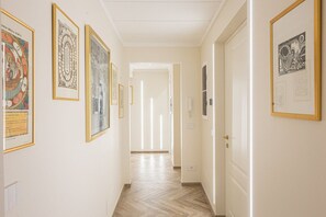 A hallway with framed artworks on the walls, a wooden floor, and a door at the end. - Refined & Elegant Apartment a few steps from Trevi Fountain (Rome)