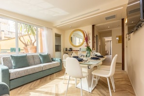 Een moderne woonkamer met een bank, eettafel, stoelen en een groot raam met uitzicht op een palmboom.