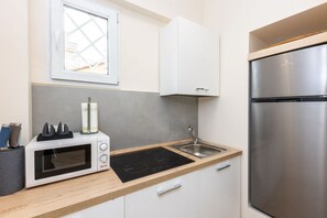 Eine kompakte Küche mit Mikrowelle, Induktionskochfeld, Edelstahlspüle und Kühlschrank.