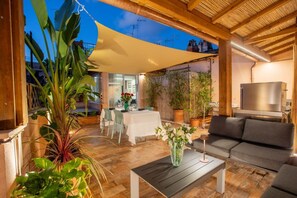 Eine Terrasse im Freien mit Tisch und Stühlen, einer Couch, Topfpflanzen und einem Fernseher.