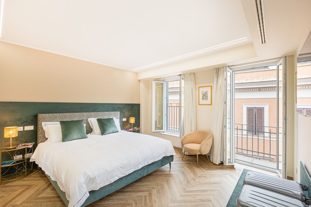 A hotel room with a large bed, a chair, a small table, and a window with a view of buildings.