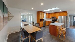 A modern kitchen with wooden cabinets, a central island, and a dining area with a table and chairs. - Spacious Home | Hot Tub | Centrally Located (Wilmington)