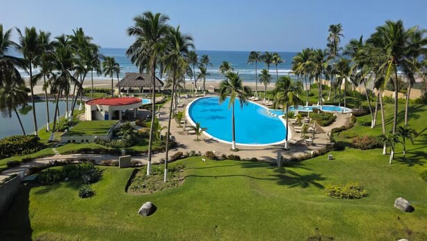 Et resort med swimmingpool, palmer, strand og havudsigt.