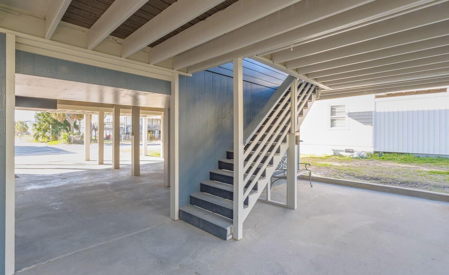 A covered outdoor area with a concrete floor, a staircase, and a view of a residential building in the background.