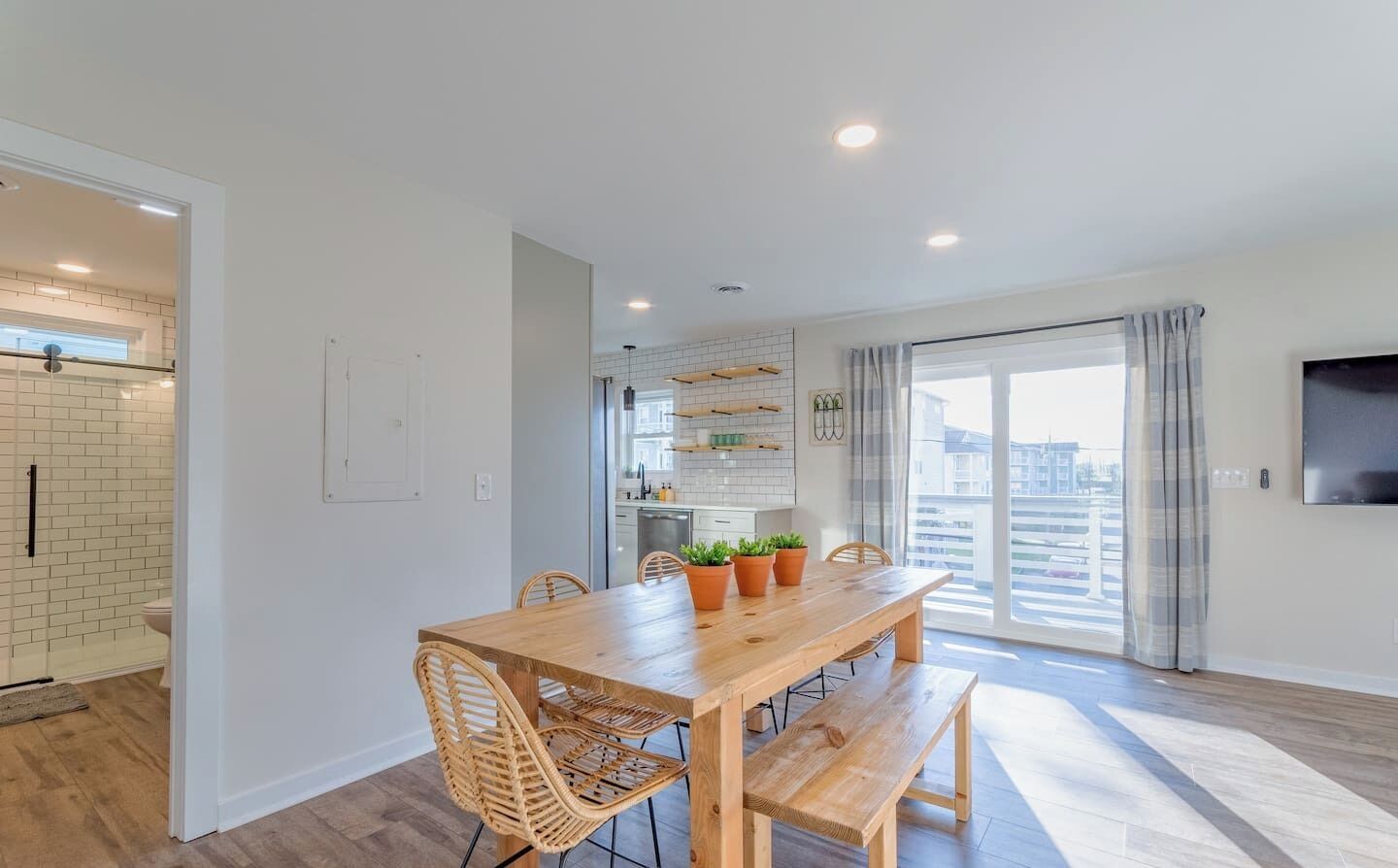 A modern kitchen with white subway tiles, a wooden dining table with chairs, and a view of the city through large windows.