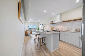 A modern kitchen with a central island, bar stools, and a view to the living area. - Community Pool | 0.2mi to Beach Access | Pier (Carolina Beach)