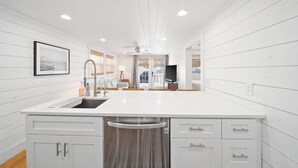 A modern kitchen with a central island, white cabinetry, and a view into the living area.