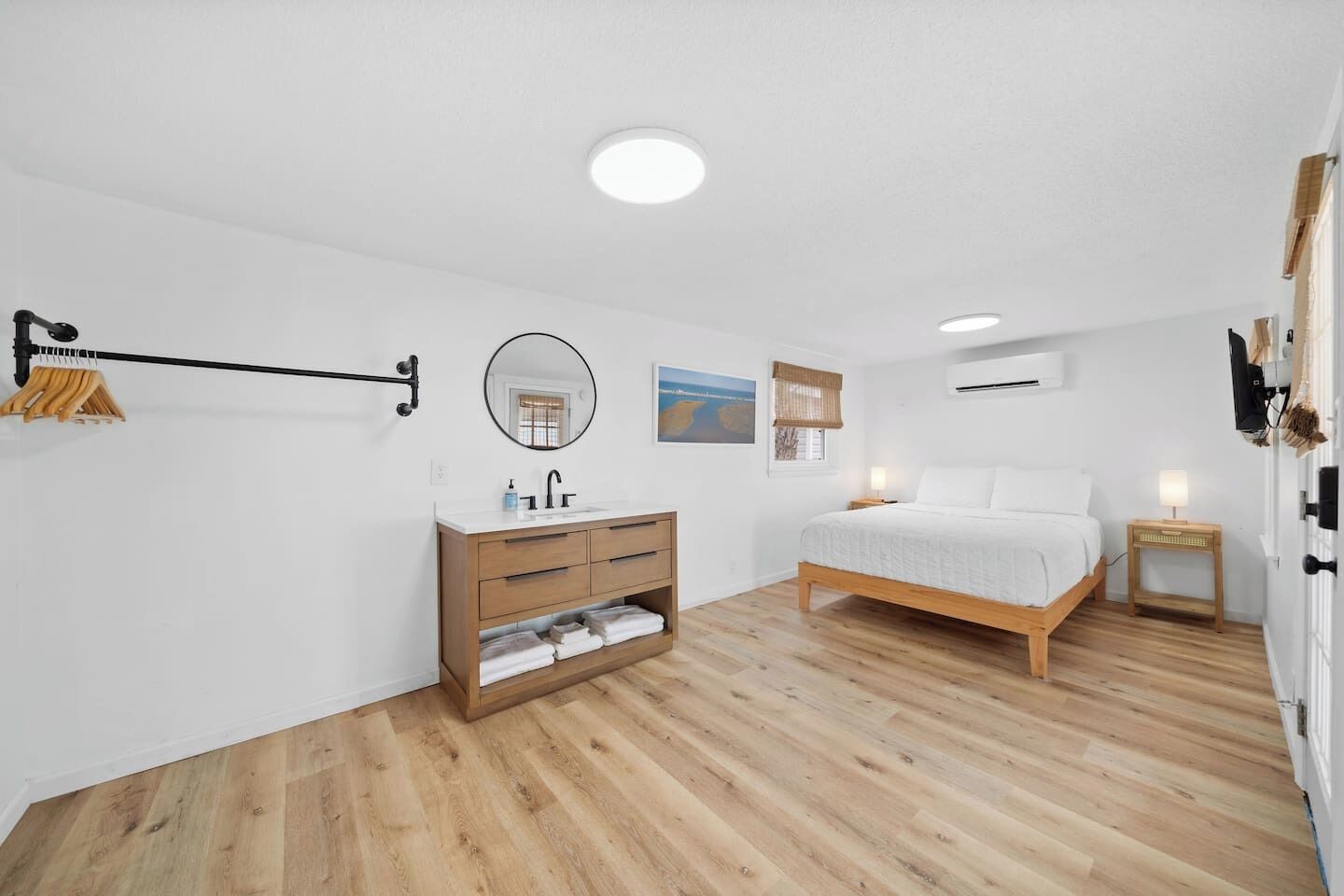 A bedroom with a wooden bed, a wooden dresser, a round mirror, a white wall, and a ceiling light.
