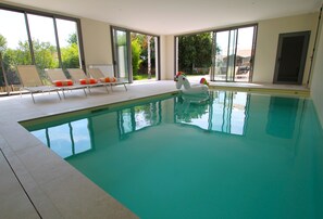 Ein Innenpool mit klaren Glaswänden, einem Schwaneinhorn-Badeartikel und Liegestühlen.