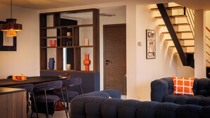 Un soggiorno moderno con un divano blu scuro, un tavolo da pranzo in legno con sedie, una libreria a parete e una scala con gradini in legno.