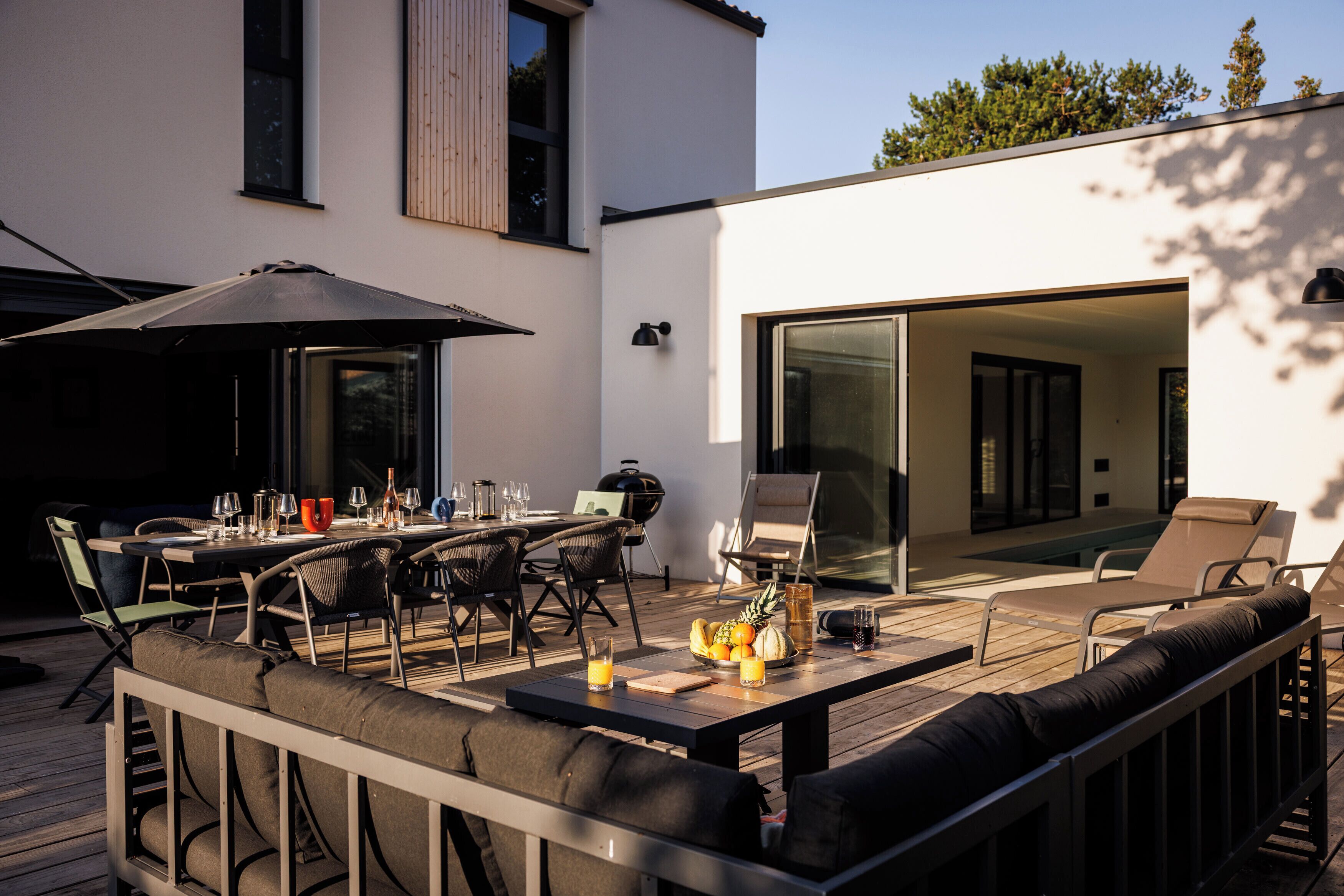 Un espacio de comedor al aire libre con una mesa dispuesta para cuatro personas, sillas alrededor y una parrilla.
