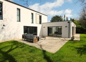 Une maison moderne dotée d’un patio, de grandes fenêtres et d’une pelouse bien entretenue.