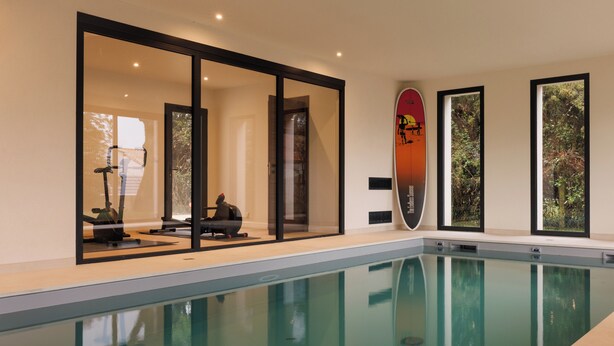 Una piscina interna con pareti in vetro trasparente, una decorazione a forma di tavola da surf e vista sul verde esterno.