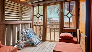 Une terrasse en bois avec un banc, un fauteuil de relaxation et une fenêtre donnant sur l’extérieur.